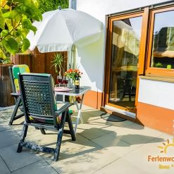 Sonnige Terrasse der Ferienwohnung Ilona in Zweibrücken mit gemütlicher Sitzgruppe, Sonnenschirm, Blumen und Zugang zum Garten – ideal zum Entspannen und Genießen.
