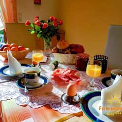 Reich gedeckter Frühstückstisch in der Ferienwohnung Ilona in Zweibrücken mit frisch gebrühtem Kaffee, Orangensaft, Brötchenkorb, Aufschnitt, Eiern und Blumen – gemütlicher Start in den Urlaubstag.
