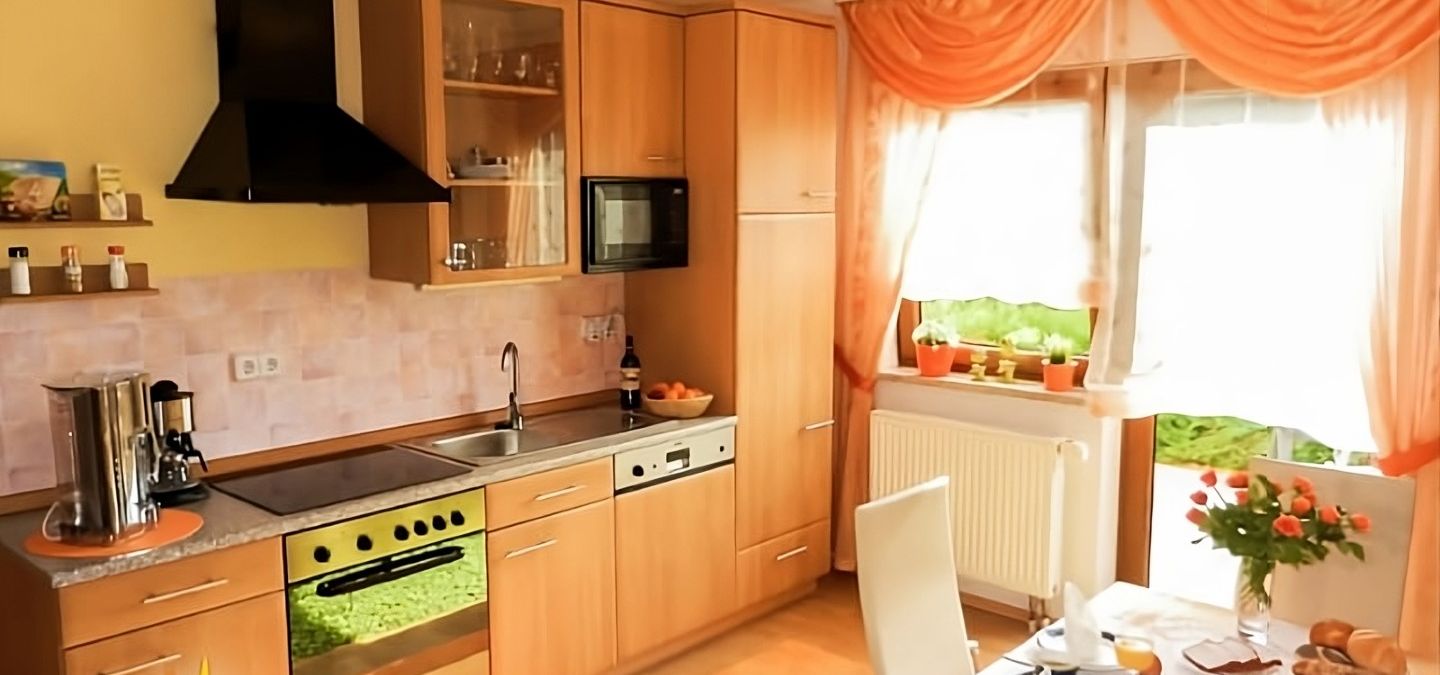 Helle, voll ausgestattete Küche der Ferienwohnung Ilona in Zweibrücken mit moderner Kochzeile, großen Fenstern und liebevoll gedecktem Frühstückstisch – ideal für gemütliche Aufenthalte.